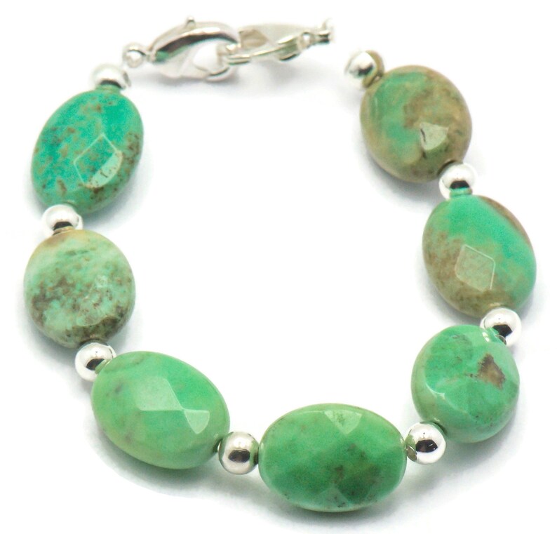 May include: A green gemstone bracelet with silver beads and a silver clasp. The bracelet is made of oval-shaped green stones with a mottled pattern.