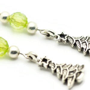 May include: A pair of silver earrings with green glass beads and a silver charm in the shape of a Christmas tree with a star on top.