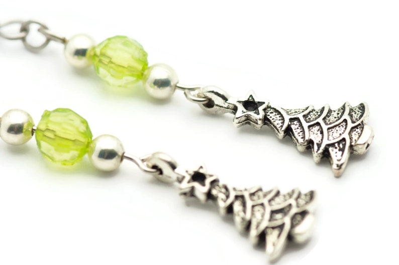 May include: A pair of silver earrings with green glass beads and a silver charm in the shape of a Christmas tree with a star on top.
