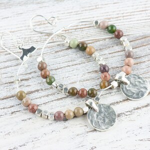 May include: A pair of silver hoop earrings with a hammered silver disc charm. The hoops are adorned with multi-colored gemstone beads.