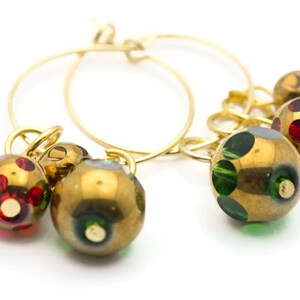 Puede incluir: Aretes de aro de oro con tres colgantes. Los colgantes son redondos y tienen una base dorada con lunares verdes y rojos.