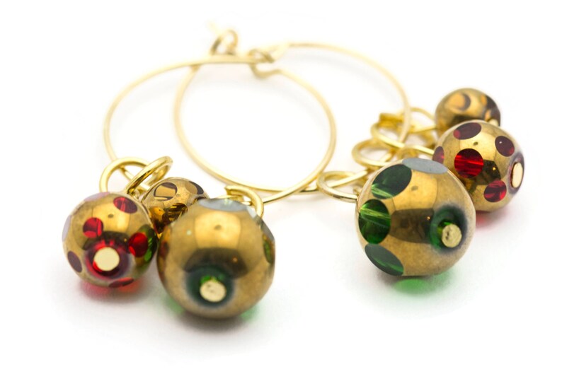 Puede incluir: Aretes de aro de oro con tres colgantes. Los colgantes son redondos y tienen una base dorada con lunares verdes y rojos.