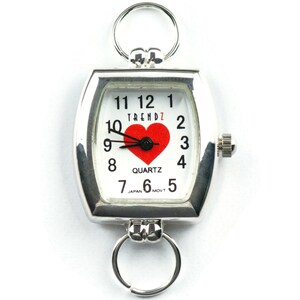 Puede incluir: Reloj de cuarzo plateado con esfera blanca con un coraz&oacute;n rojo y n&uacute;meros negros. El reloj tiene forma rectangular con bordes redondeados y dos llaveros. El reloj dice "TRENDZ" y "QUARTZ".
