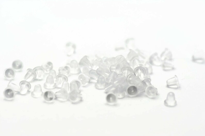 May include: A pile of clear plastic earring backs. The backs are small and round, with a small hole in the center. They are designed to be used with stud earrings.