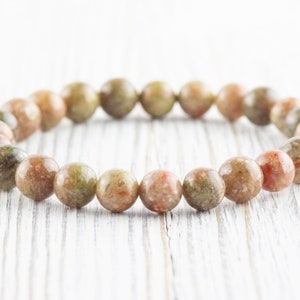 May include: A bracelet made of green, brown, and pink speckled stone beads.