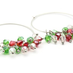 May include: Silver hoop earrings with red, green, and clear crystal beads dangling from the hoops.