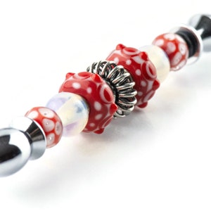 Peut inclure: Un bracelet &agrave; breloques argent&eacute; avec des perles de verre &agrave; motifs rouges et blancs et une perle d'espacement argent&eacute;e.