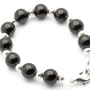 Puede incluir: Una pulsera con grandes cuentas negras brillantes intercaladas con cuentas m&aacute;s peque&ntilde;as de color plateado. La pulsera se asegura con un cierre plateado. Las cuentas tienen aproximadamente 1,3 cm de di&aacute;metro, creando un contraste llamativo.