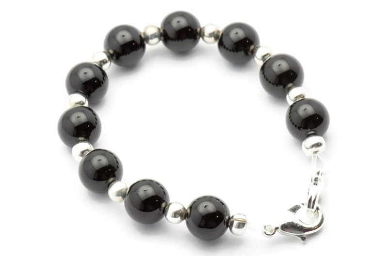 Puede incluir: Una pulsera con grandes cuentas negras brillantes intercaladas con cuentas m&aacute;s peque&ntilde;as de color plateado. La pulsera se asegura con un cierre plateado. Las cuentas tienen aproximadamente 1,3 cm de di&aacute;metro, creando un contraste llamativo.