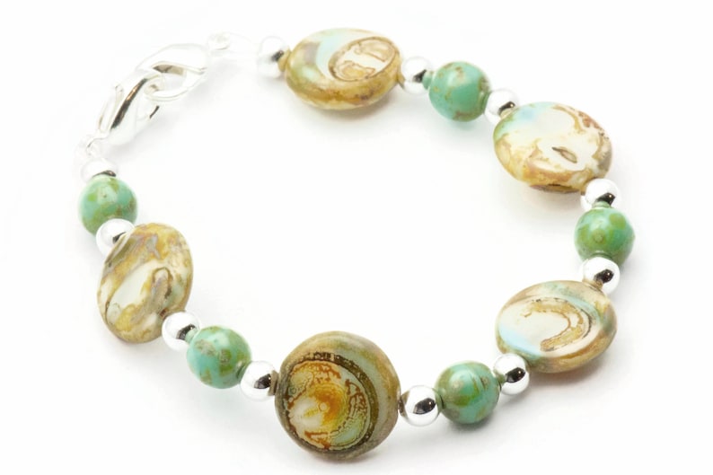 Op de afbeelding: Een armband met zilveren en groene kralen. De kralen zijn rond en hebben een marmerpatroon. De armband heeft een zilveren sluiting.