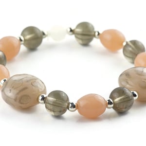 May include: A bracelet made of light brown, dark brown, and peach-coloured beads. The beads are oval-shaped and have a smooth, polished finish.
