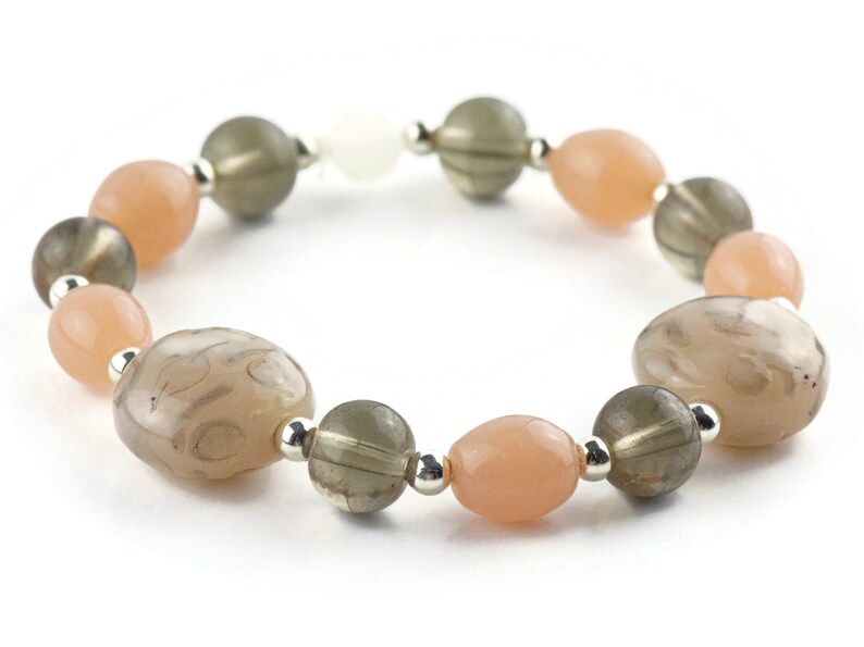 May include: A bracelet made of light brown, dark brown, and peach-coloured beads. The beads are oval-shaped and have a smooth, polished finish.