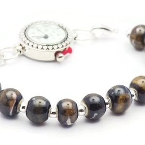 May include: A brown and black ceramic bead bracelet with a silver watch attached. The watch face is white with black hands and numbers.