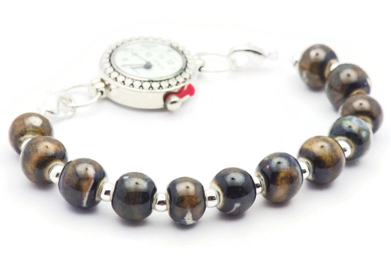 May include: A brown and black ceramic bead bracelet with a silver watch attached. The watch face is white with black hands and numbers.