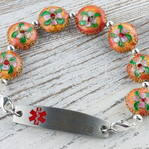 May include: A medical alert bracelet with a silver chain and orange and green floral beads. The bracelet has a silver tag that reads "Type 1 Diabetes".