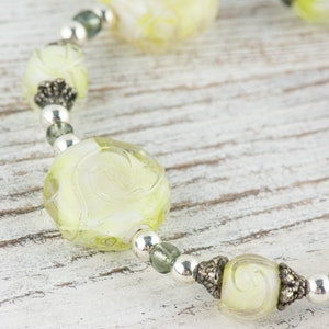 Peut inclure: Gros plan sur un collier de perles en verre vert et blanc avec des accents argent&eacute;s. Les perles sont rondes et pr&eacute;sentent un motif en spirale.