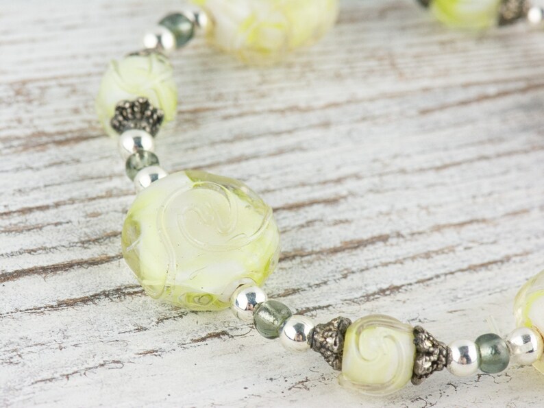 Peut inclure: Gros plan sur un collier de perles en verre vert et blanc avec des accents argent&eacute;s. Les perles sont rondes et pr&eacute;sentent un motif en spirale.