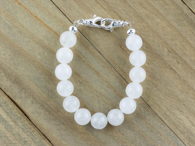 May include: A white gemstone bracelet with a silver clasp. The bracelet is made of round, smooth beads.