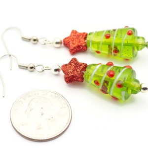 Op de afbeelding: Een paar groene en rode glazen kerstboom oorbellen met zilveren haakjes. Elke oorbel heeft een rode ster en rode en witte strepen.