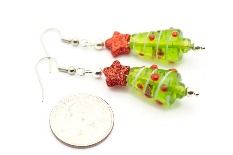 Op de afbeelding: Een paar groene en rode glazen kerstboom oorbellen met zilveren haakjes. Elke oorbel heeft een rode ster en rode en witte strepen.