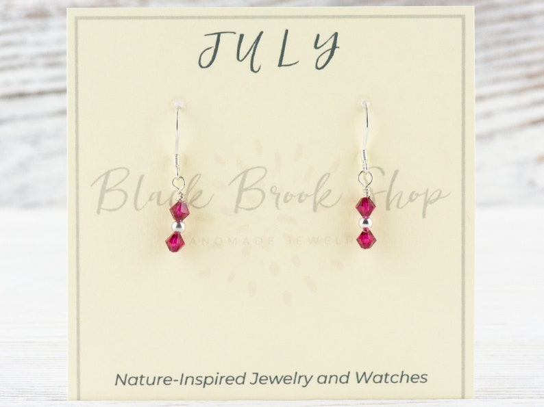 Puede incluir: Pendientes de plata con dos cuentas de cristal rosa. Los pendientes est&aacute;n en una tarjeta que dice "Julio" y "Black Brook Shop Joyer&iacute;a hecha a mano".
