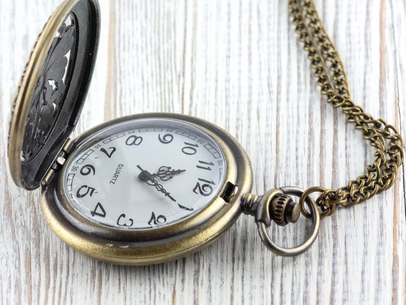 May include: Antique brass pocket watch with a white face, black numerals, and ornate hands. The watch has a hinged cover with a decorative design and a matching chain. The watch is open, revealing the time.