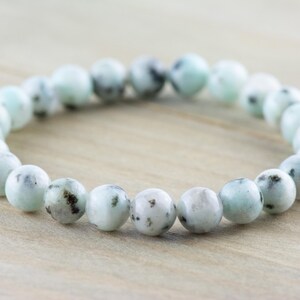 Puede incluir: Un brazalete hecho de cuentas redondas de color azul claro y blanco con motas. Las cuentas son lisas.