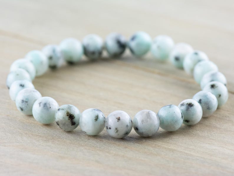 Puede incluir: Un brazalete hecho de cuentas redondas de color azul claro y blanco con motas. Las cuentas son lisas.
