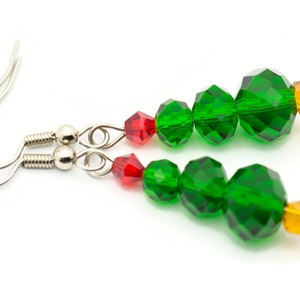 May include: A pair of silver dangle earrings with green and red crystal beads shaped like a Christmas tree. The earrings have a silver hook closure.