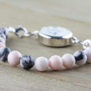 May include: A silver watch with a white face attached to a bracelet made of pink and black beads.