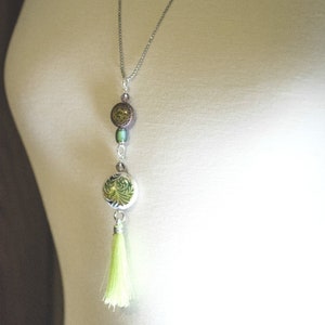 May include: A silver chain necklace with a green and brown patterned pendant and a lime green tassel.