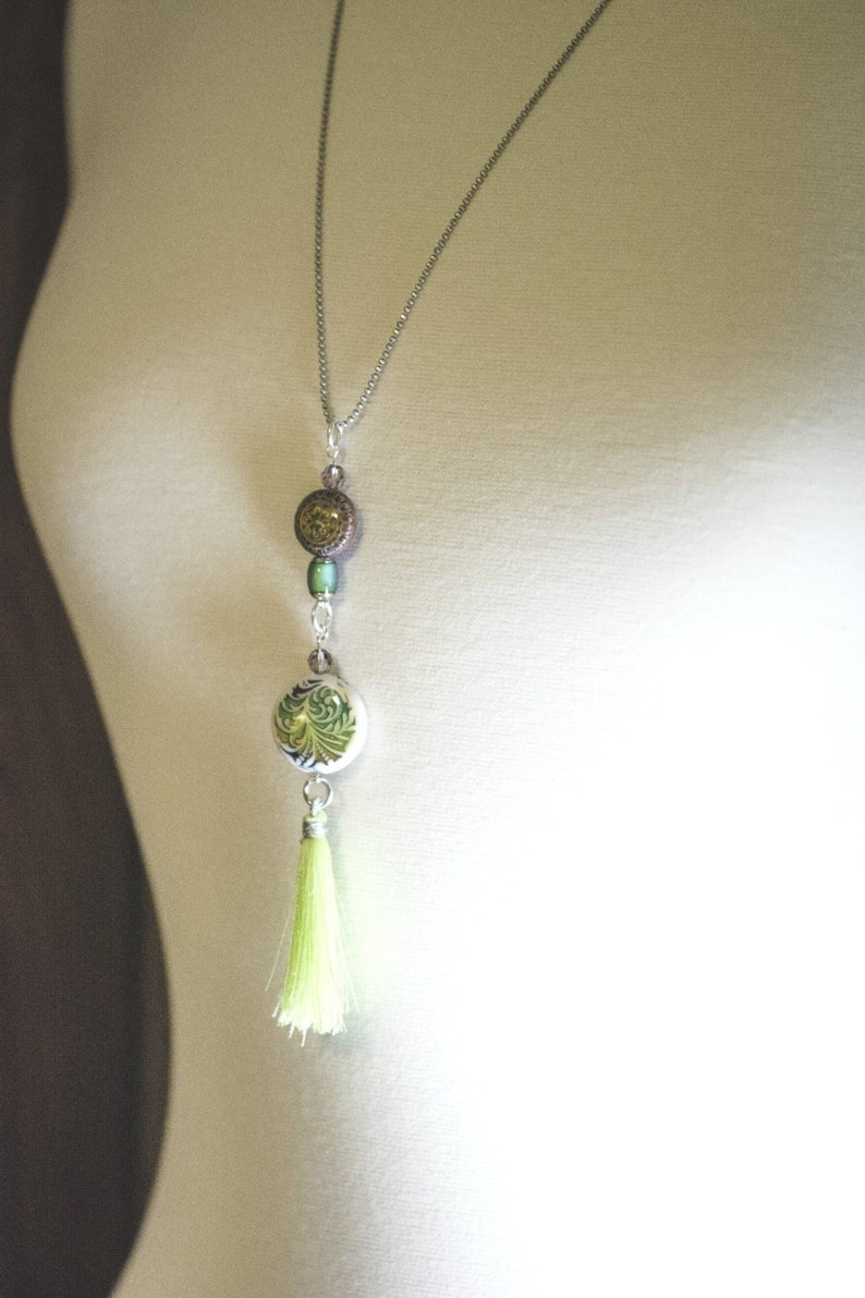 May include: A silver chain necklace with a green and brown patterned pendant and a lime green tassel.