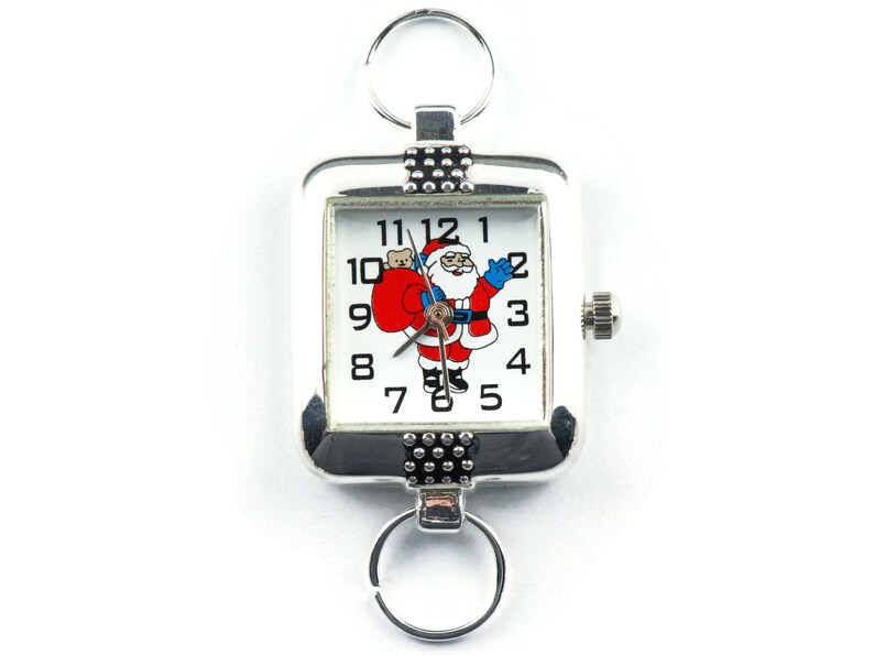 Pu&ograve; includere: Un orologio quadrato argentato con un quadrante bianco e un design di Babbo Natale. L'orologio ha un anello di perline nere attorno al bordo del quadrante e un portachiavi argentato.