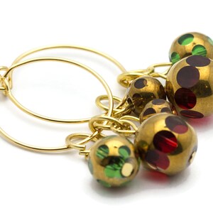 May include: Gold hoop earrings with a cluster of dangling beads. The beads are gold with red and green polka dots.