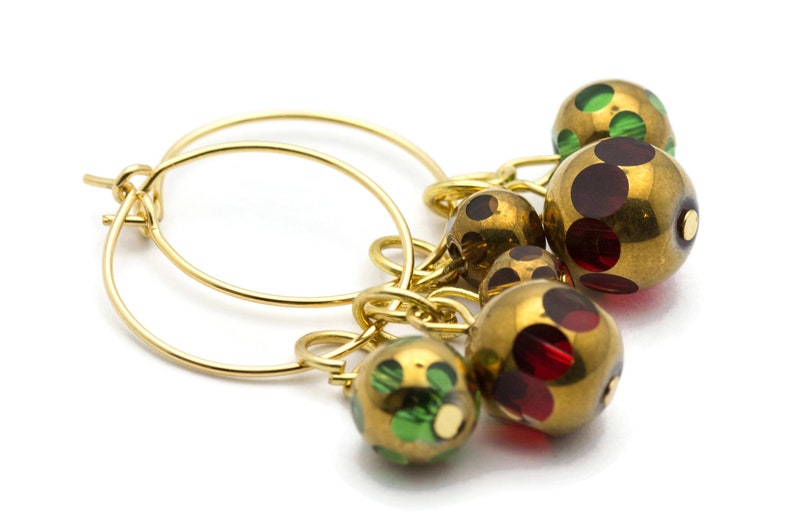 May include: Gold hoop earrings with a cluster of dangling beads. The beads are gold with red and green polka dots.