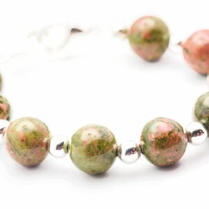May include: A bracelet made of green and pink speckled beads with silver spacers.