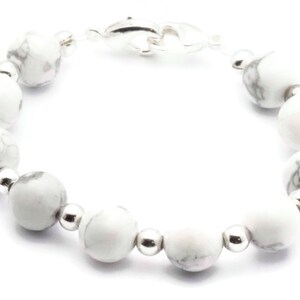 May include: A bracelet featuring white and grey marbled stone beads, interspersed with small silver-coloured beads. The bracelet is secured with a dolphin-shaped clasp. The beads are strung on a clear cord.