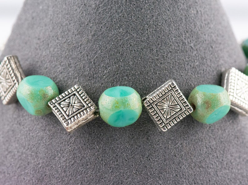 Pu&ograve; includere: Un braccialetto turchese e argento con perline quadrate e accenti decorativi.