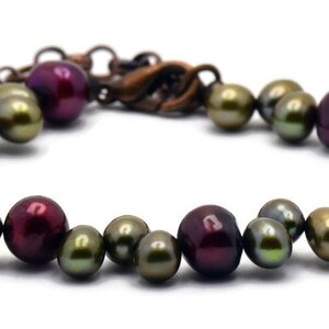May include: A bracelet made of dark red and green iridescent pearls. The bracelet has a copper clasp.