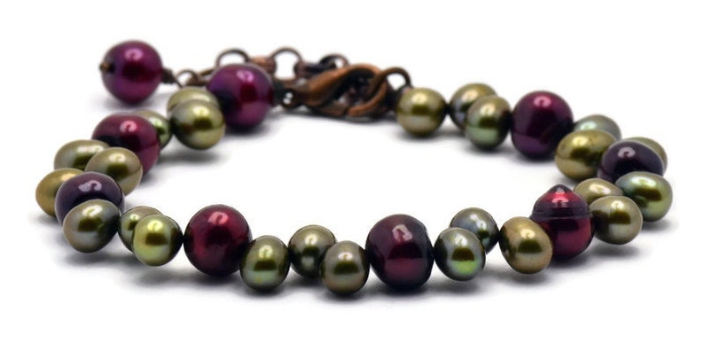 May include: A bracelet made of dark red and green iridescent pearls. The bracelet has a copper clasp.