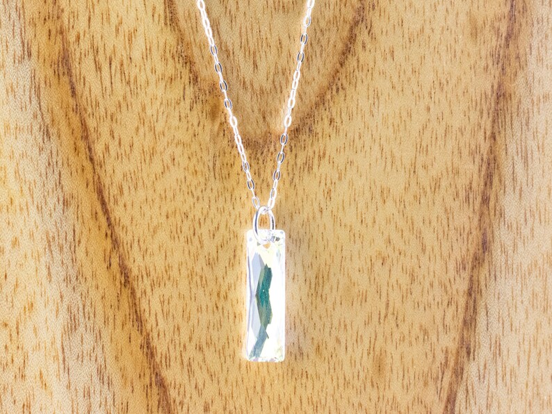 Pu&ograve; includere: Una collana con catena d'argento con un ciondolo rettangolare con una pietra verde e bianca.