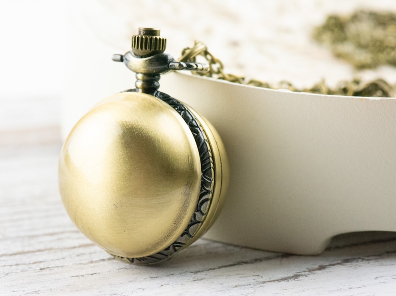 May include: A gold-toned pocket watch with a chain, the watch has a round face and a decorative design around the edge.