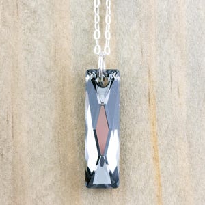 Pode incluir: Um colar de corrente de prata com um pingente de cristal facetado retangular longo. O cristal &eacute; transparente com um toque de cinza e um centro cinza mais escuro.