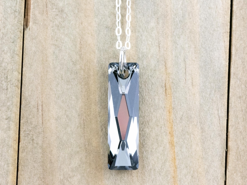 Pode incluir: Um colar de corrente de prata com um pingente de cristal facetado retangular longo. O cristal &eacute; transparente com um toque de cinza e um centro cinza mais escuro.