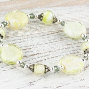 Peut inclure: Un bracelet avec des perles de verre vertes et blanches et des accents argent&eacute;s.
