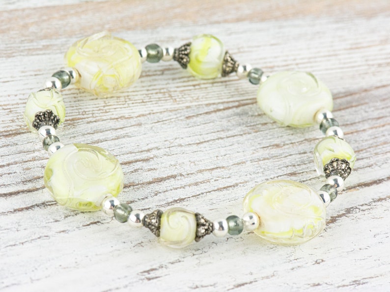 Peut inclure: Un bracelet avec des perles de verre vertes et blanches et des accents argent&eacute;s.