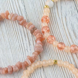 May include: Three bracelets made of natural stones. The first bracelet is made of light peach-coloured sunstone beads. The second bracelet is made of peach-coloured glass beads with gold flecks. The third bracelet is made of light peach-coloured glass beads with gold accents.