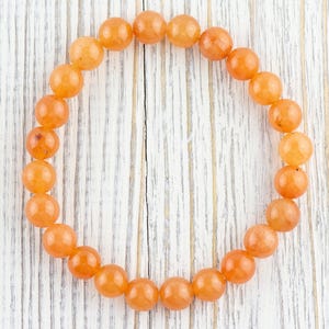 May include: A bracelet made of orange carnelian beads. The beads are round and smooth, and the bracelet is strung on a clear elastic cord.
