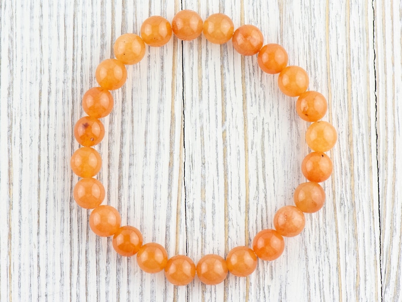May include: A bracelet made of orange carnelian beads. The beads are round and smooth, and the bracelet is strung on a clear elastic cord.