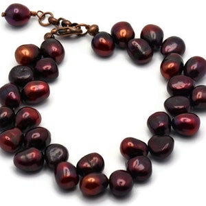 May include: A dark red freshwater pearl bracelet with a copper clasp. The pearls are irregular in shape and have a high luster.